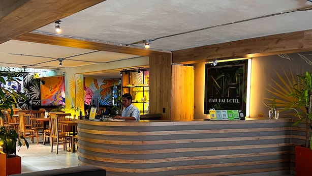 A reception area with a curved wooden counter, a man at the desk, and a sign that reads "NAUTILICAL HOTEL". - Hotel Natural (Medellín)