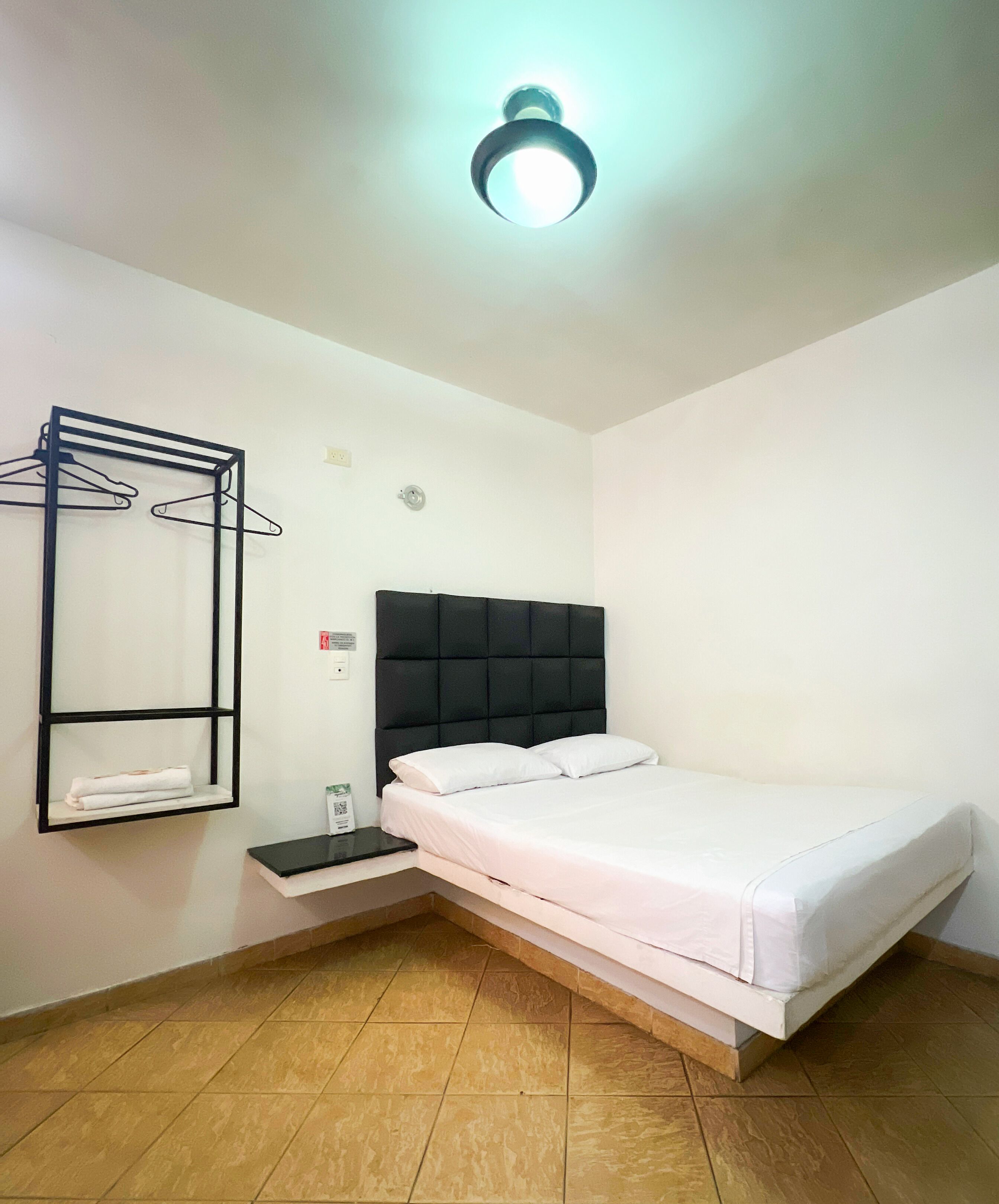 A neatly arranged bedroom with a bed, a wall-mounted shelf with towels, and a ceiling light.