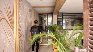 A modern hallway with a minimalist design, featuring a large mirror, potted plants, and a wooden ceiling beam. - Hotel Natural (Medellín)