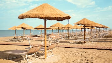 Een privéstrand, wit zand, ligstoelen aan het strand, parasols