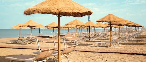 Een privéstrand, wit zand, ligstoelen aan het strand, parasols