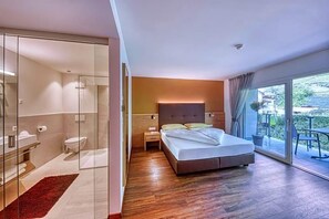 Un dormitori modern amb un llit gran, un bany amb dutxa de vidre i un balcó amb vistes.