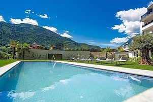 Piscina con sillones de descanso, montañas al fondo y cielo despejado.