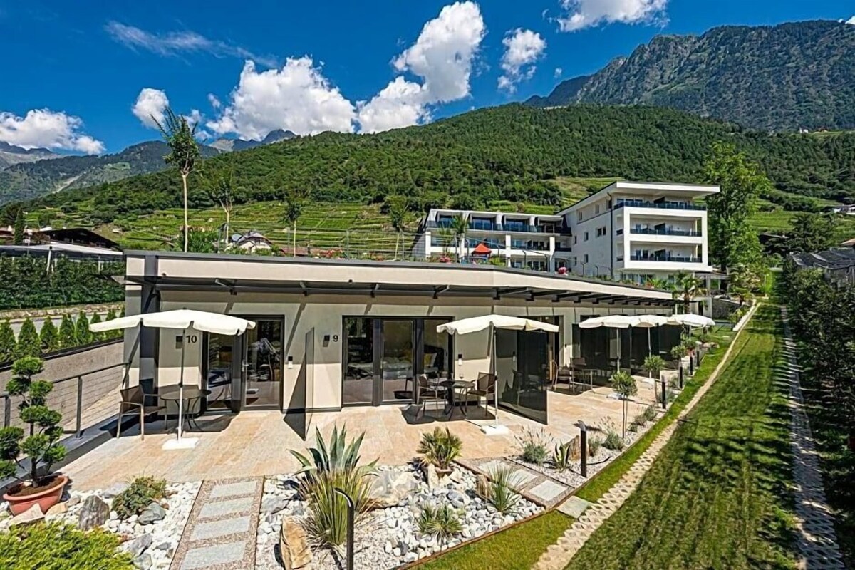 A modern building with a patio area, outdoor seating, and a view of a mountainous landscape.