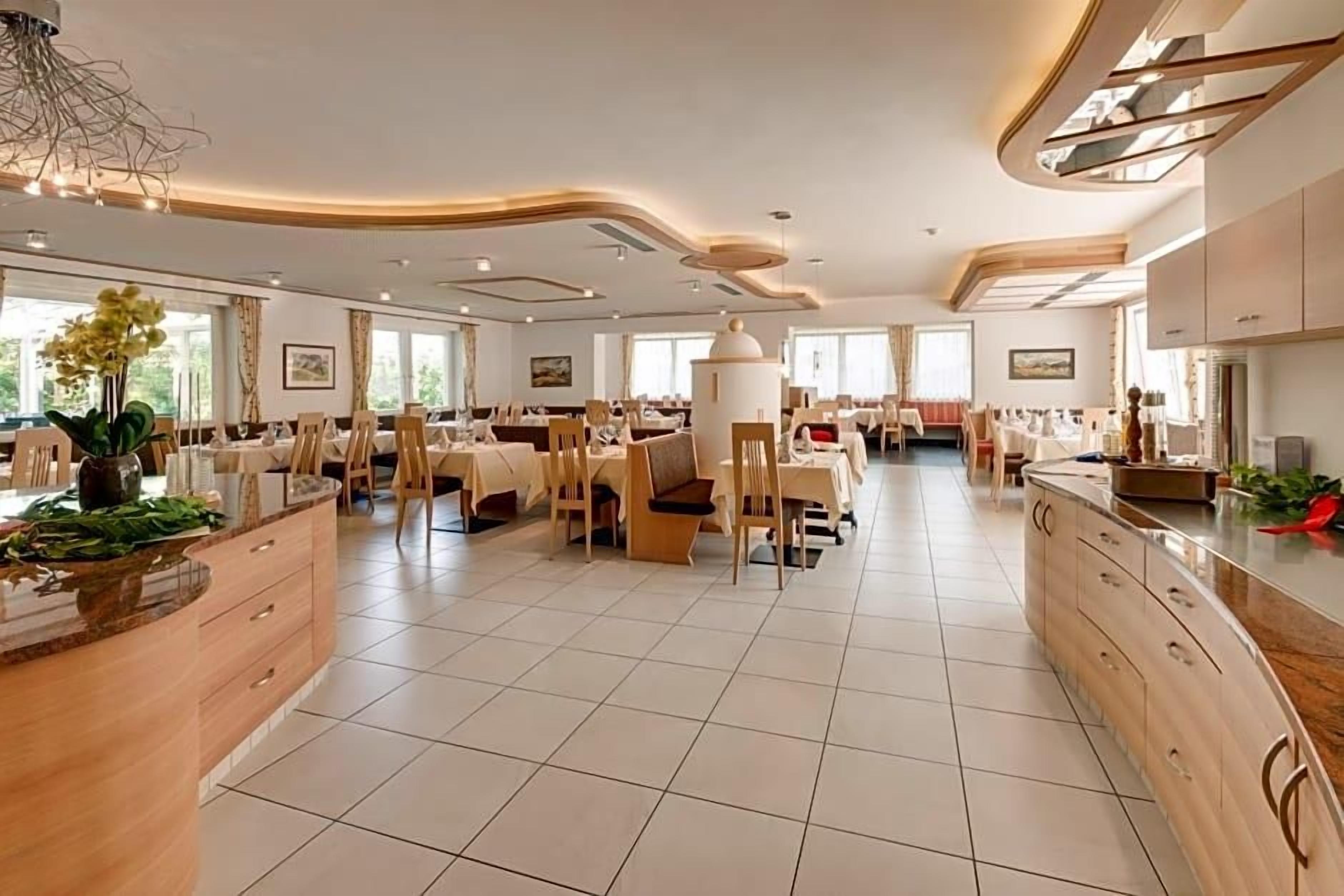 Ein großzügiger Essbereich mit mehreren Tischen und Stühlen, eine zentrale Kochinsel mit Blumenvase und ein modernes Decken-Design.