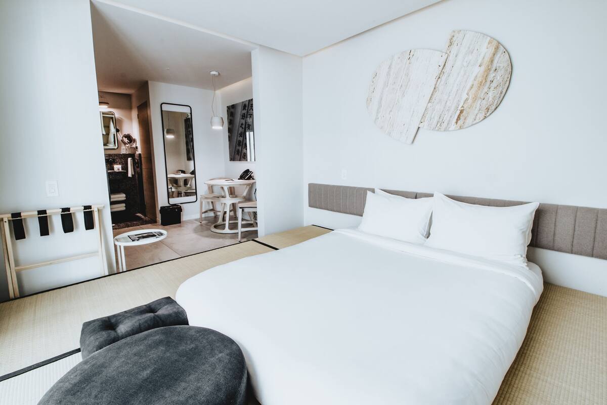 A modern hotel room with a large bed, a small desk, and a mirror.