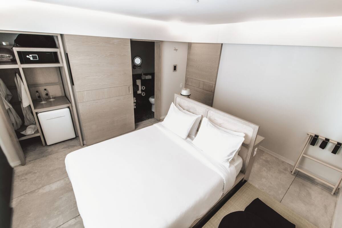 A modern hotel room with a large bed, a wardrobe, a small desk, and a mirror.