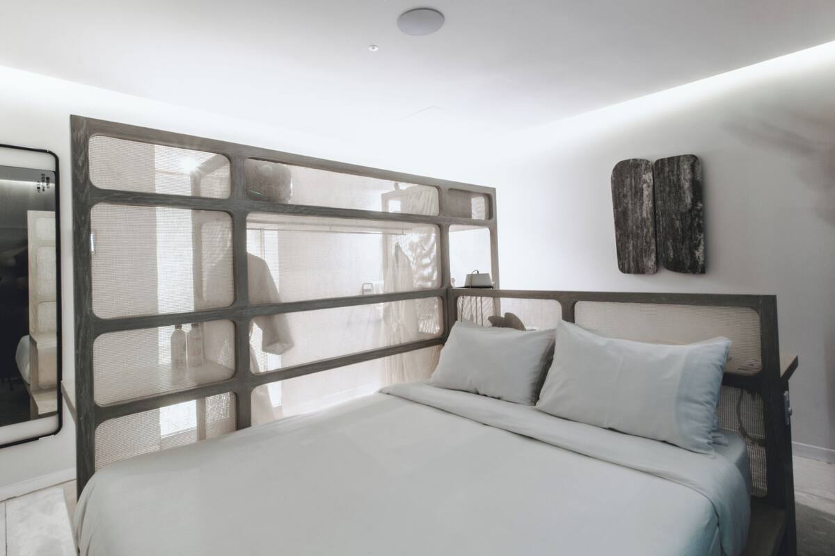 A modern bedroom with a large bed, a headboard with a geometric design, and a wall-mounted artwork.