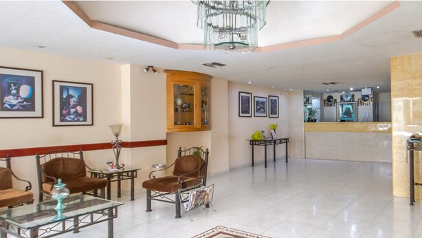 A hotel lobby with a reception desk, seating area with chairs, a coffee table, and a potted plant. - Hotel Astromundo (Reynosa)