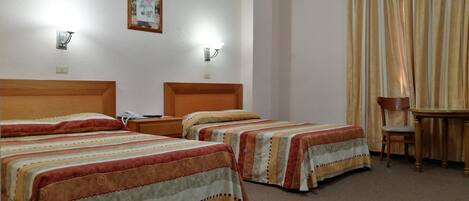 A hotel room with two beds, a desk, a chair, and a window with curtains.