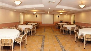 A conference room with multiple round tables and chairs, a projector screen, and a tiled floor. - Hotel Astromundo (Reynosa)