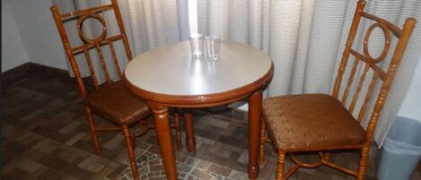 A dining area with a round table and four wooden chairs, a tiled floor, and a curtain in the background.