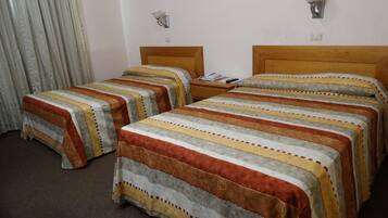Habitación de hotel con dos camas, cada una con ropa de cama a rayas, cabecero de madera y mesita de noche con lámpara.