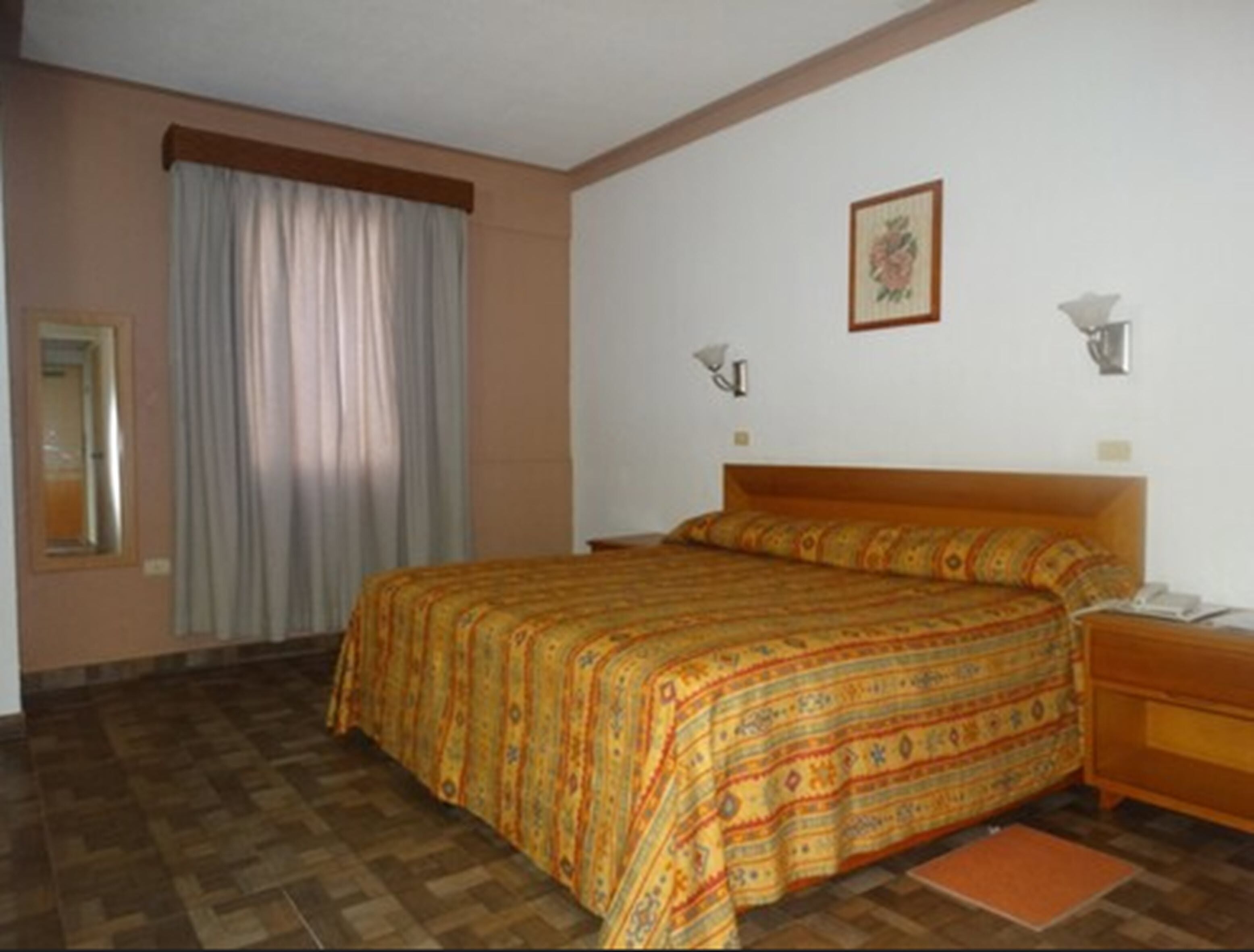 Un dormitorio con una colcha estampada, un cabecero de madera, una mesita de noche, una lámpara y un cuadro enmarcado en la pared.