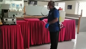 A person in a blue shirt and black pants standing in a room with red tablecloths, a coffee machine, and a large fan on the ceiling. - Hotel Astromundo (Reynosa)