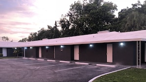 A row of motel rooms with a parking lot in front.