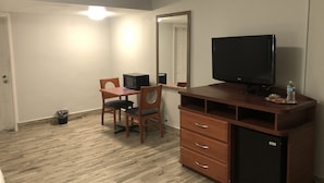 A hotel room with a wooden desk, a television, a mirror, and a small refrigerator.