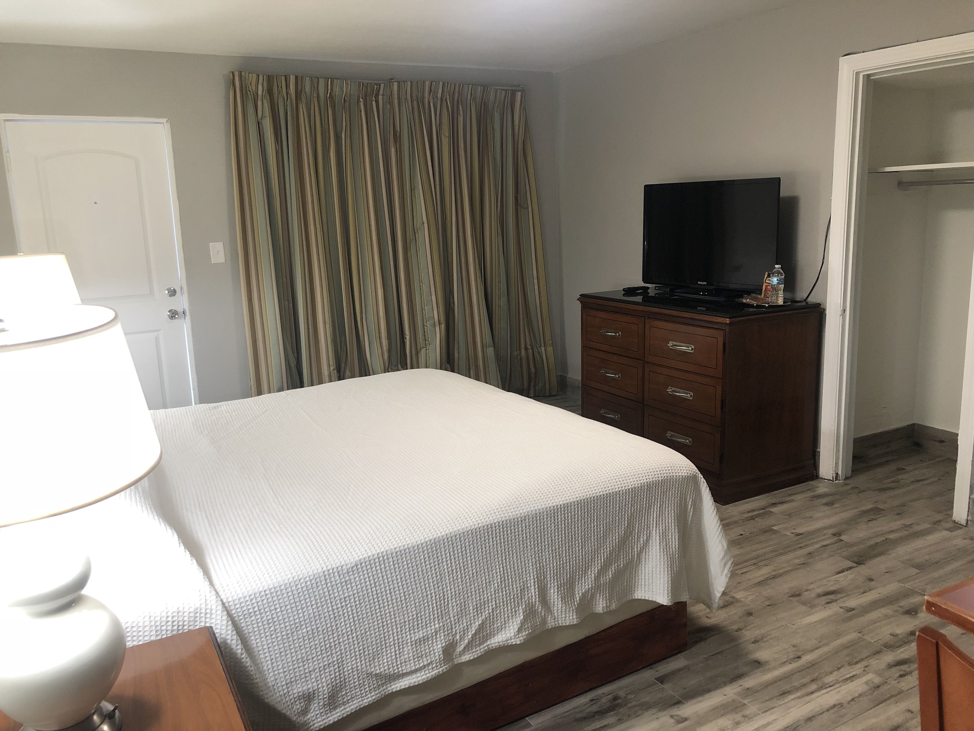 A hotel room with a bed, a wooden dresser, a television, and a curtain.