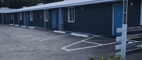 A row of motel rooms with blue doors and white trim, a parking lot, and a garden area with flowers.
