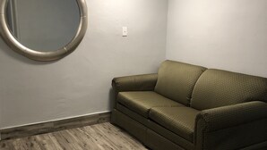 A room with a wooden floor, a green sofa, a round mirror, and a ceiling light.