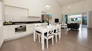 A modern kitchen with white cabinetry, a dining area with white chairs, and a living area with a sofa and TV. - Centro Garden (Willemstad)