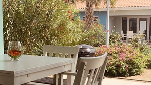 A patio with a white table and chairs, a grill, and lush greenery. - Centro Garden (Willemstad)