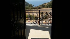 Eine offene Tür, die zu einem Balkon mit Blick auf das Meer und die Hügel führt.