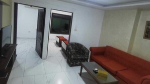 A living room with a sofa, a coffee table, a TV, and a patterned chair. - Marj Alhamam Furnished Suites (Amman)