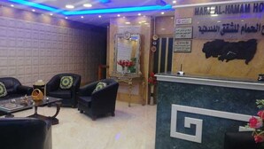 A hotel reception area with a marble counter, two sofas with patterned cushions, and a decorative mirror. - Marj Alhamam Furnished Suites (Amman)