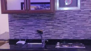 A modern kitchen with wooden cabinets, a black countertop, a built-in sink, and a backsplash with a mosaic tile design. - Marj Alhamam Furnished Suites (Amman)
