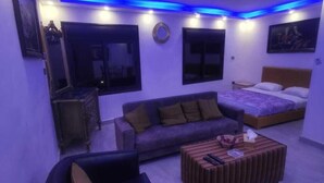 A modern living room with a sofa, a coffee table, and a bed. - Marj Alhamam Furnished Suites (Amman)