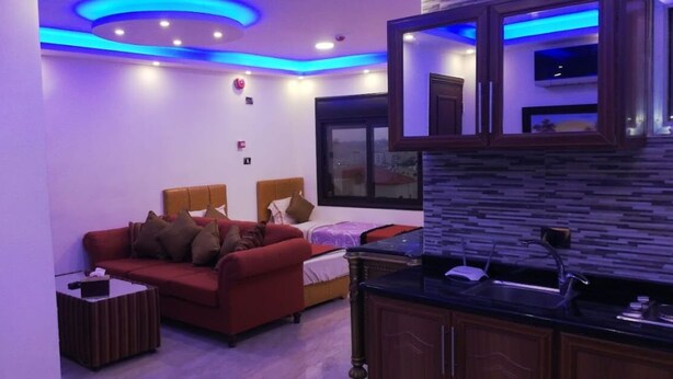 A modern living room with a red sofa, a small coffee table, and a bed with a wooden headboard. - Marj Alhamam Furnished Suites (Amman)