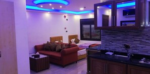 A modern living room with a red sofa, a small coffee table, and a bed with a wooden headboard. - Marj Alhamam Furnished Suites (Amman)