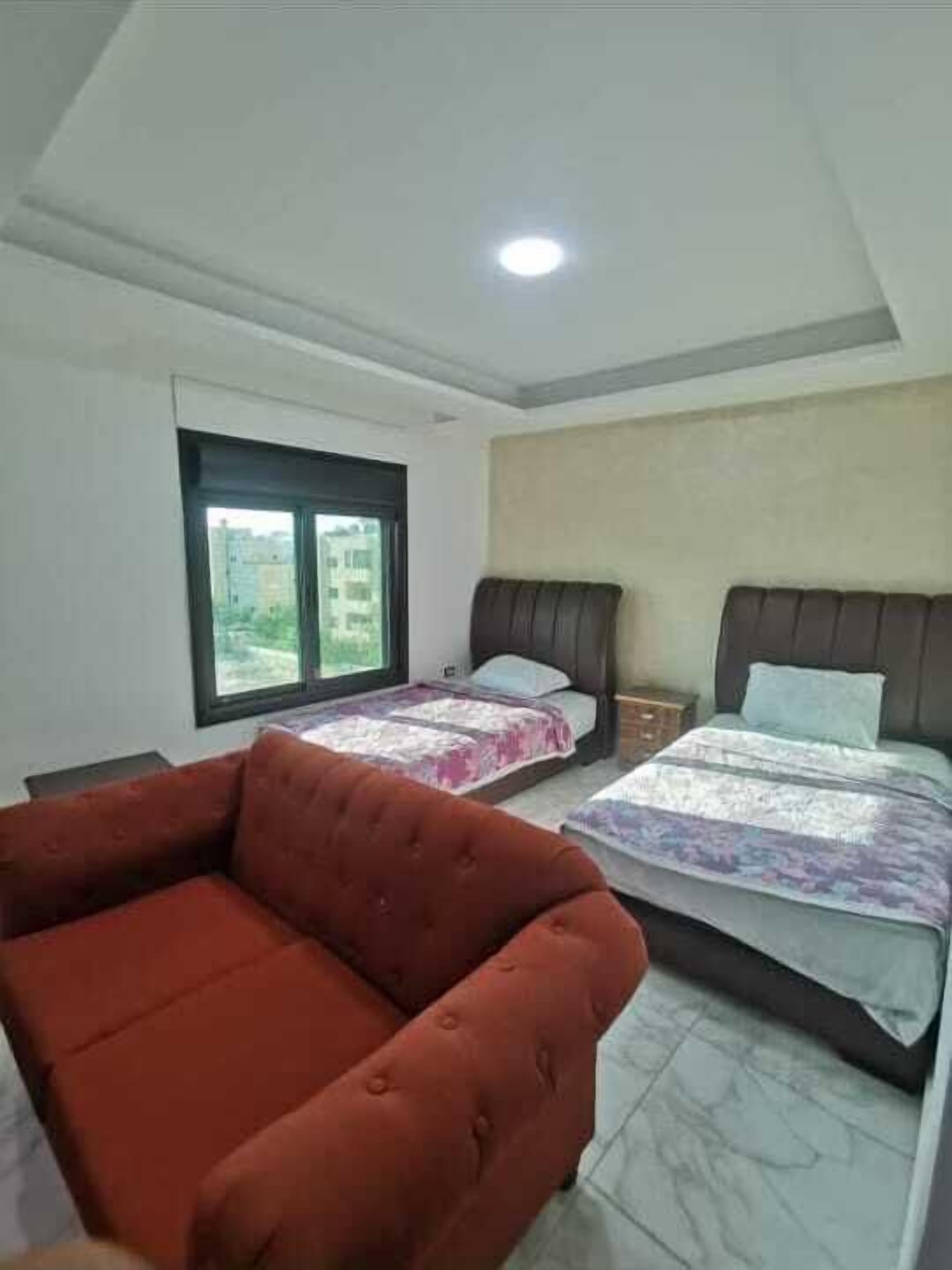 A bedroom with two beds, a red sofa, and a window with a view of buildings.