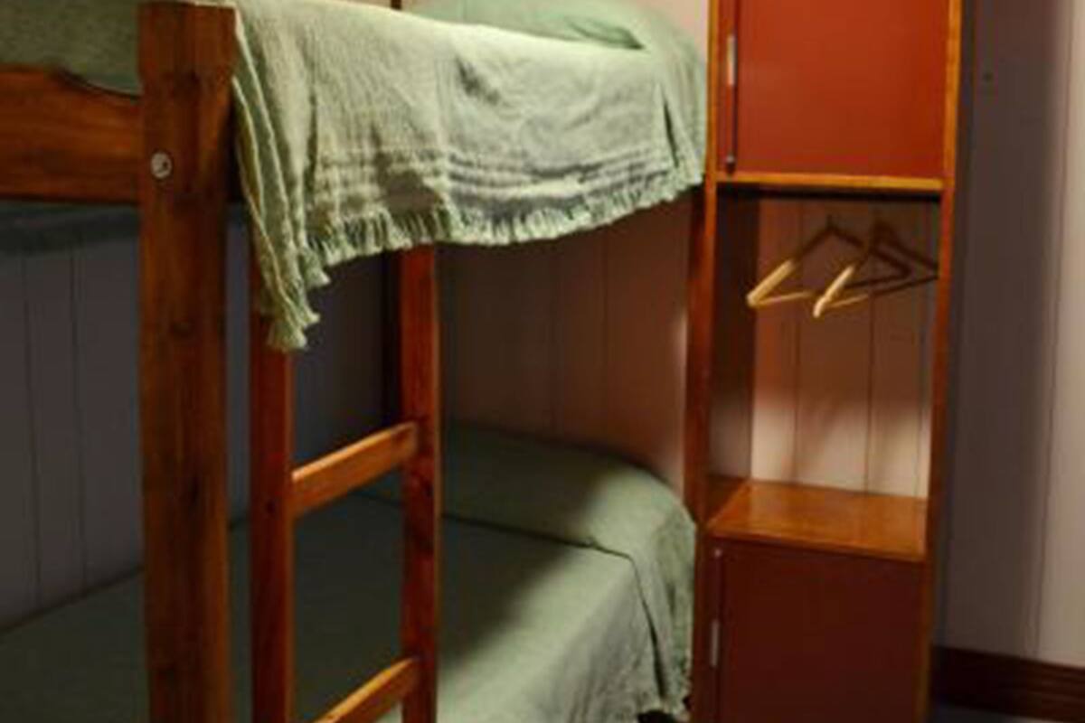 A bunk bed with a green blanket, a wooden shelf unit, and a hanging rack.