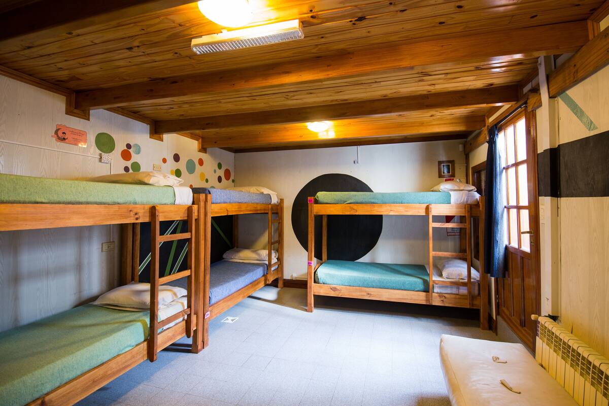 A room with bunk beds, wooden ceiling beams, a radiator, and a window with curtains.
