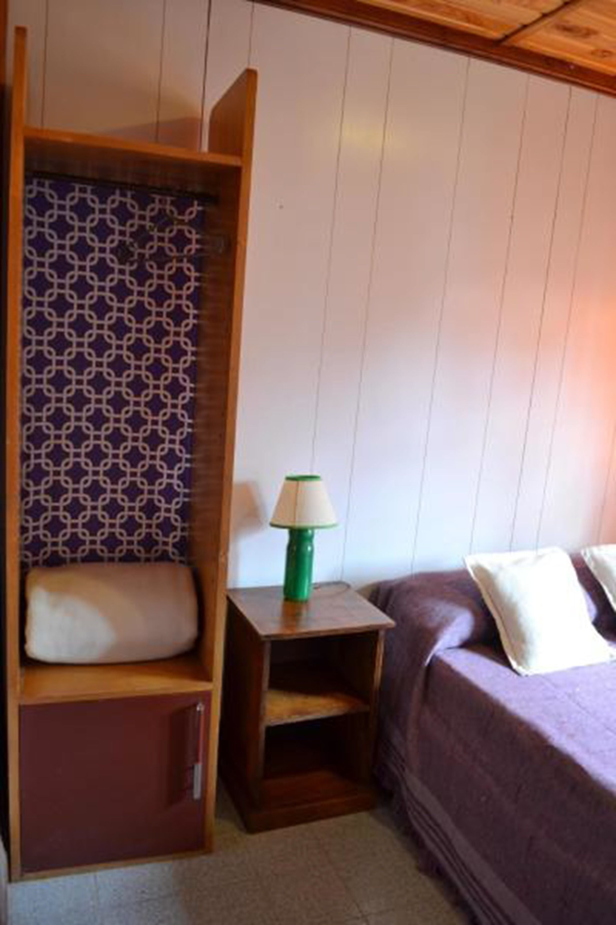 Ein Zimmer mit einem Bett, einem Nachttisch mit Stoffmuster und einem kleinen Tisch mit Lampe.