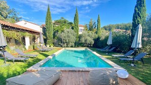 Piscina rectangular con cubierta de madera al frente, rodeada de sillas de descanso y sombrillas.
