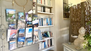 Una habitación con una estantería llena de libros y folletos de viajes, una estatua decorativa de Buda y una lámpara de mimbre.