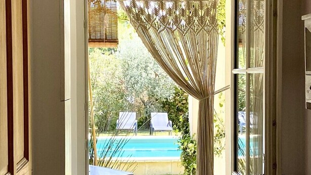 Un acceso a un área de piscina con un cortinero de macramé, asientos exteriores y vistas despejadas a la piscina.