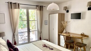 Un dormitorio con una cama, un escritorio y una silla. Hay una ventana con cortinas, un televisor en la pared y una lámpara.