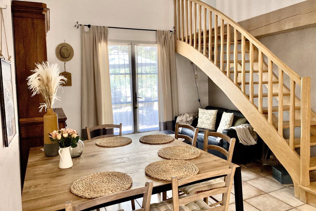 Un coin repas avec une table en bois, des sets de table en fibres tressées et un escalier en bois.