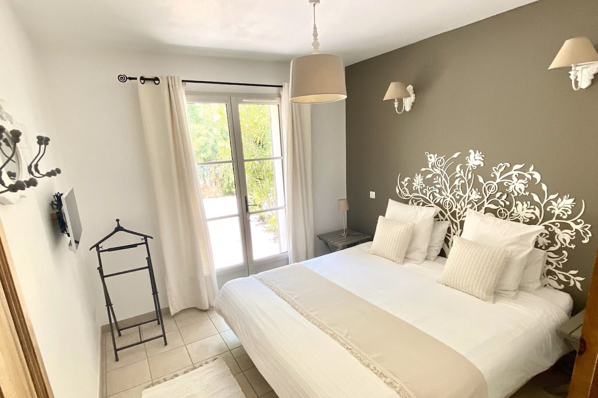 Une chambre avec un grand lit, une fenêtre avec des rideaux, une table de chevet avec une lampe et un luminaire fixé au mur.