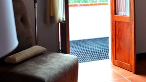 Quarto com sofá, luminária, porta de madeira e vista para o verde lá fora.