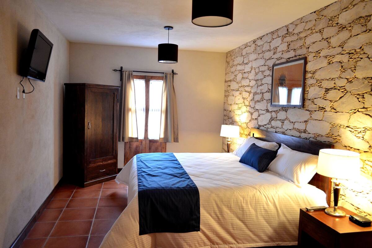 Een slaapkamer met een bed, nachtkastje, lamp, televisie en een stenen muur.