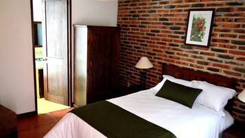 A bedroom with a brick wall, a bed with white bedding, a green throw, and a wooden headboard.