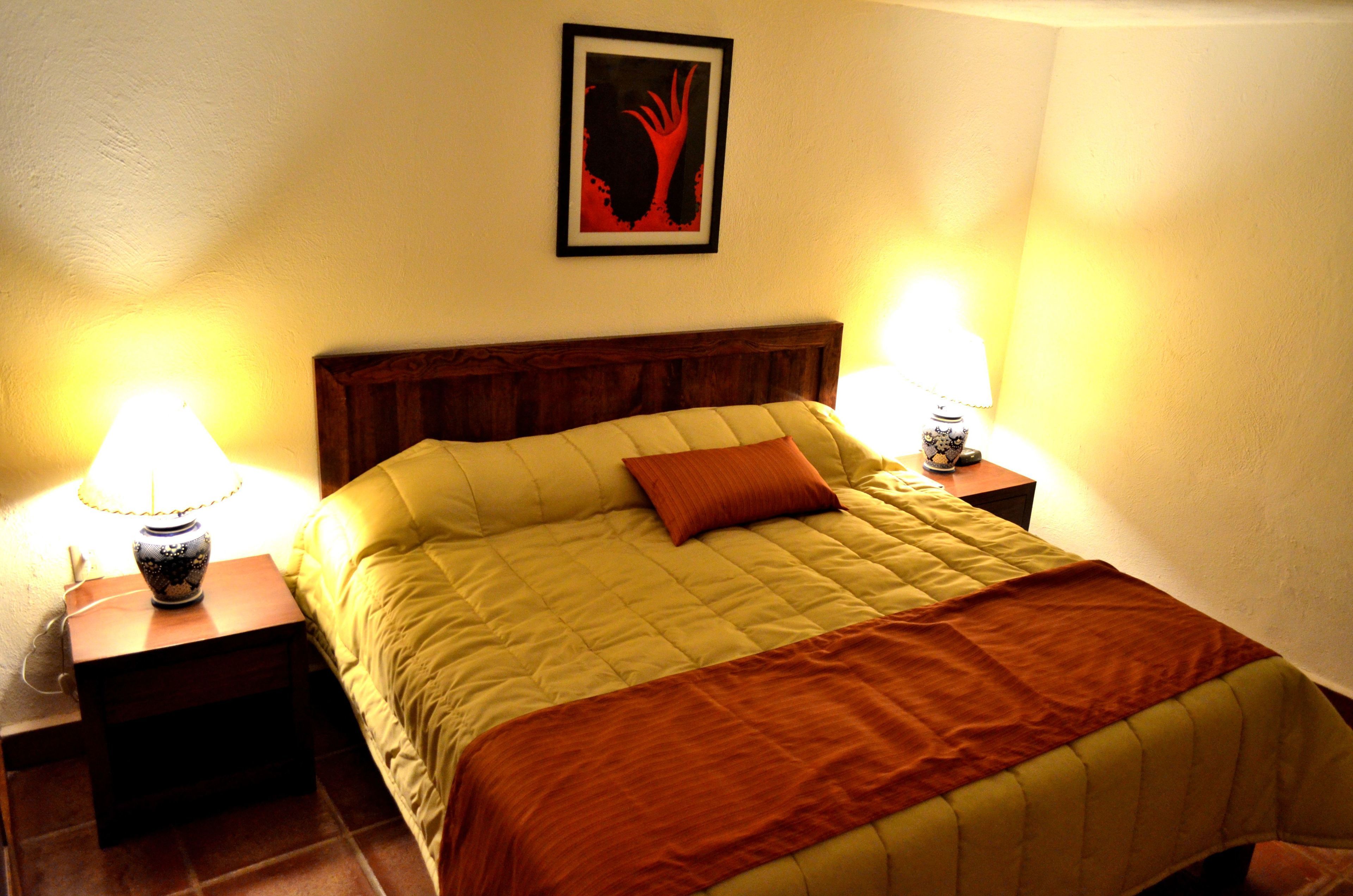 Ein Bett mit Holz-Kopfteil, zwei Nachttischlampen und ein gerahmtes Bild an der Wand.