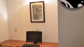 Quarto com uma escrivaninha, computador, cadeira e um quadro na parede.