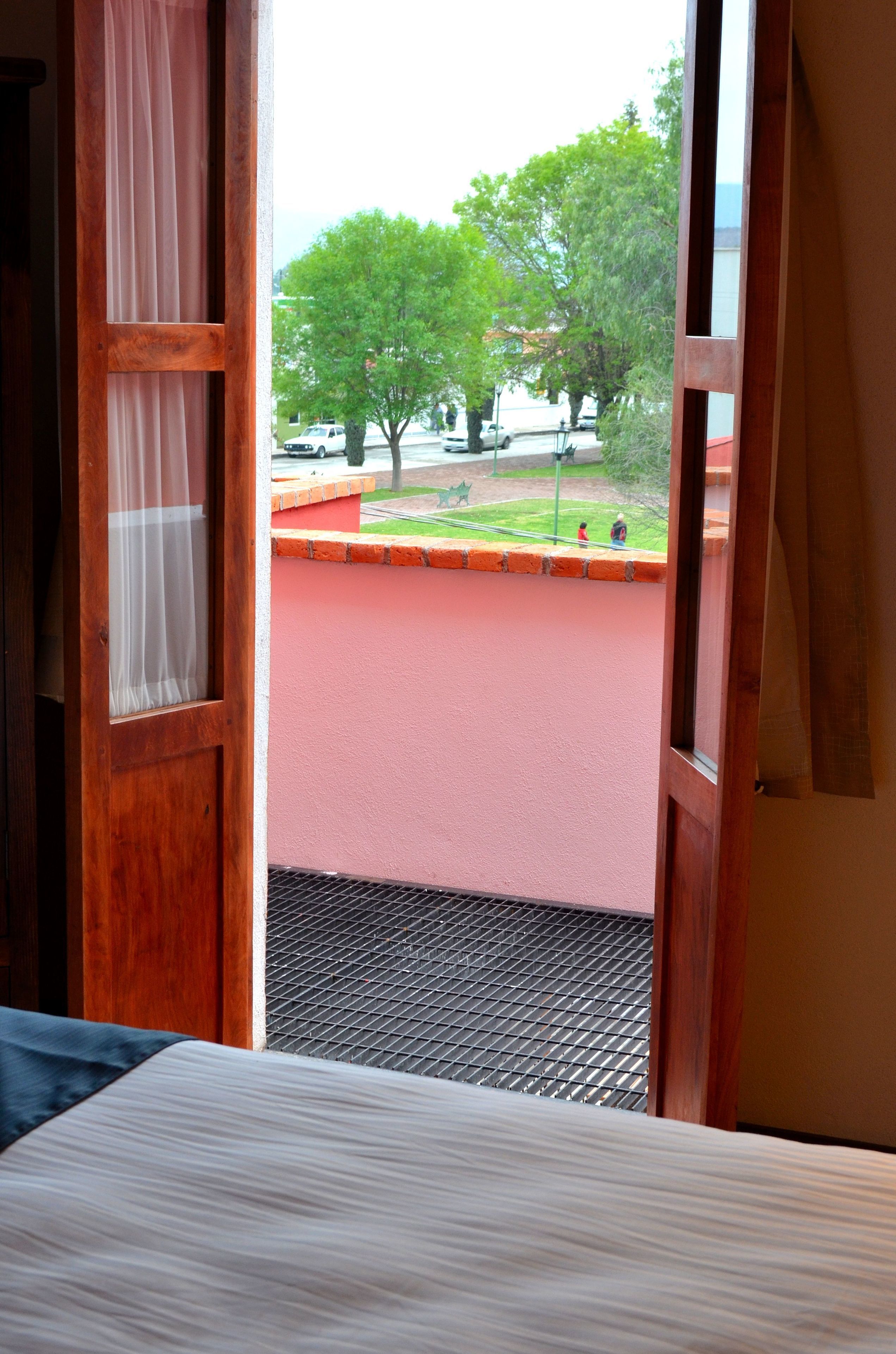 A room with a bed, a window with a view of a courtyard, and a door with a curtain.
