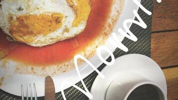 Un plato de desayuno con huevos revueltos y salsa de tomate, una taza de café y cubiertos sobre una mesa con un mantel individual.